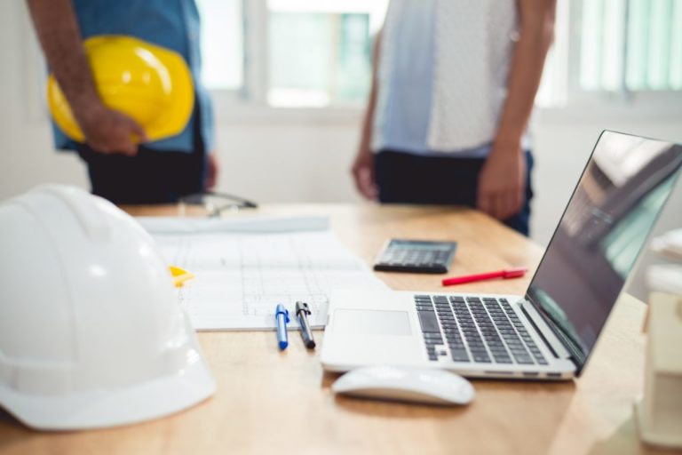 Desk with construction plans, safety helmet, and laptop computer