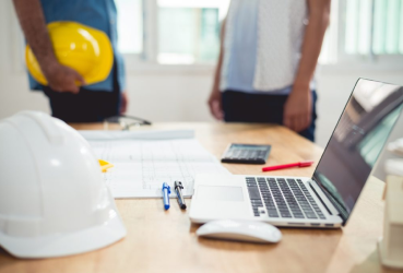 Work desk with laptop computer, construction hardhat and blueprints